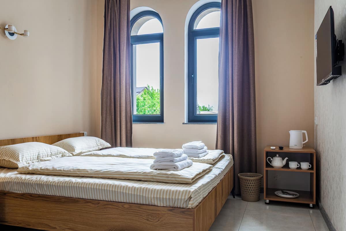 A room with two beds, a wooden nightstand with a kettle, cups, and a basket.