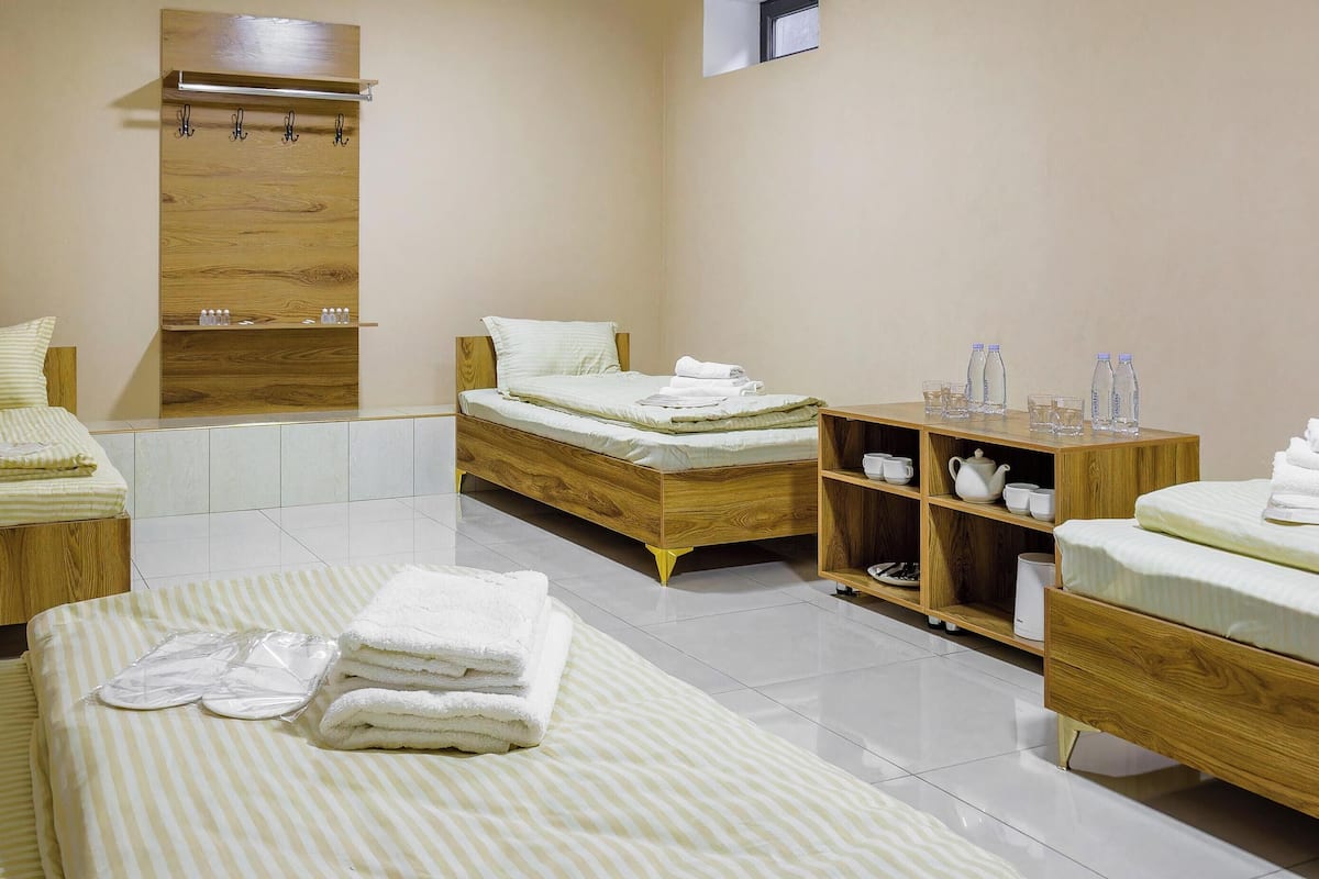 A hotel room with two wooden beds, a wooden wardrobe, a small wooden shelf with toiletries, and a tiled floor.