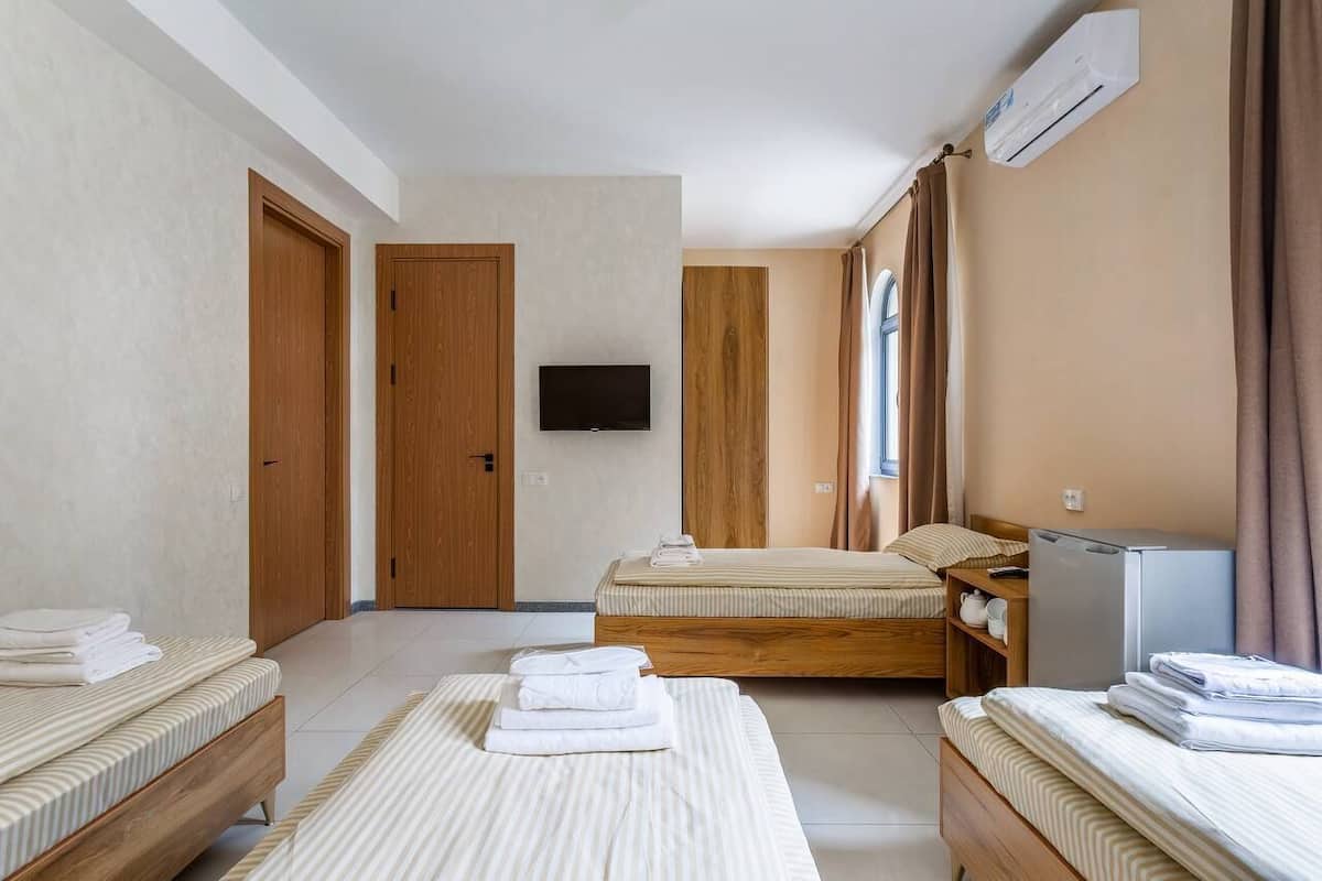 A hotel room with two beds, a TV, a refrigerator, and a window with curtains.