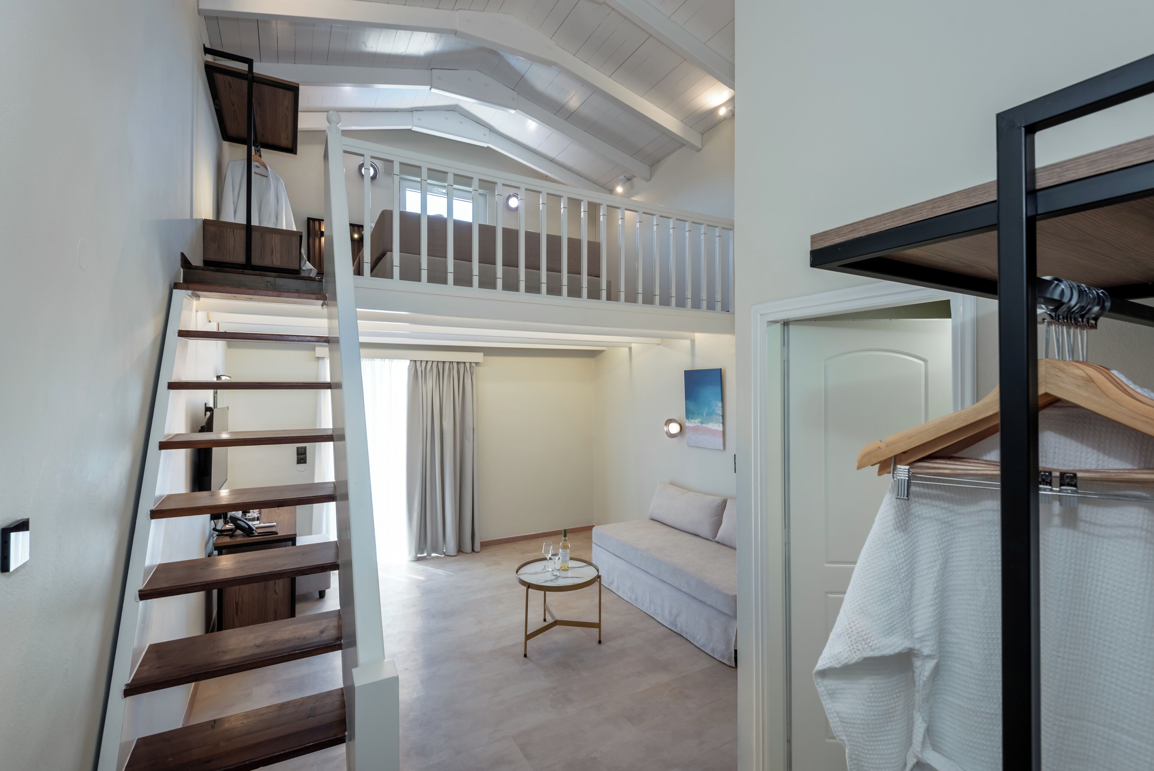 A modern interior with a loft bedroom, a staircase, a small round table, and a hanging coat rack.