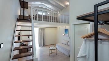 A modern interior with a loft bedroom, a staircase, a small round table, and a hanging coat rack.