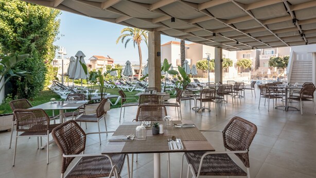 Un área de café al aire libre con mesas, sillas, sombrillas y vista al mar.
