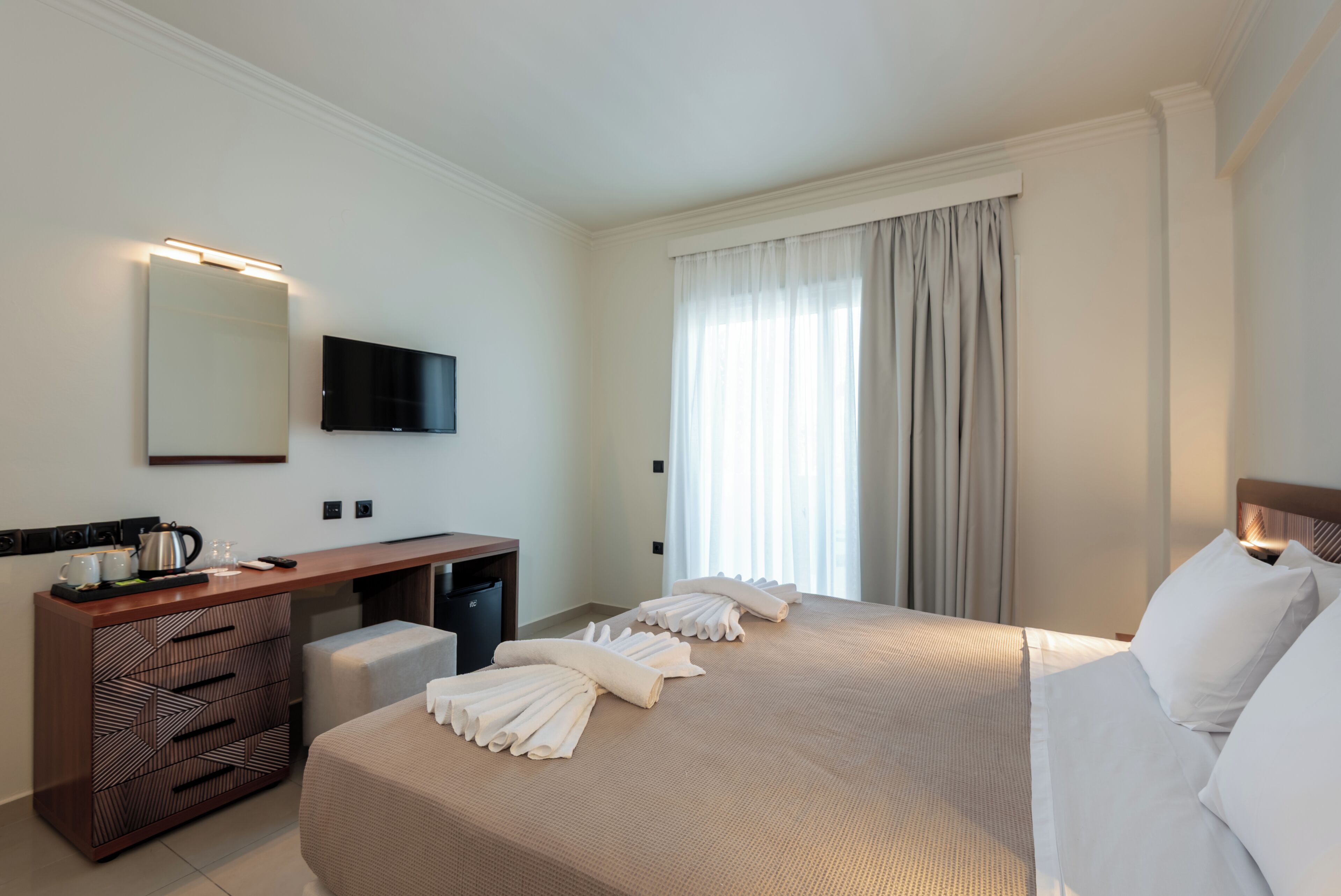 Habitación de hotel con cama, escritorio, televisión y ventana con cortinas.