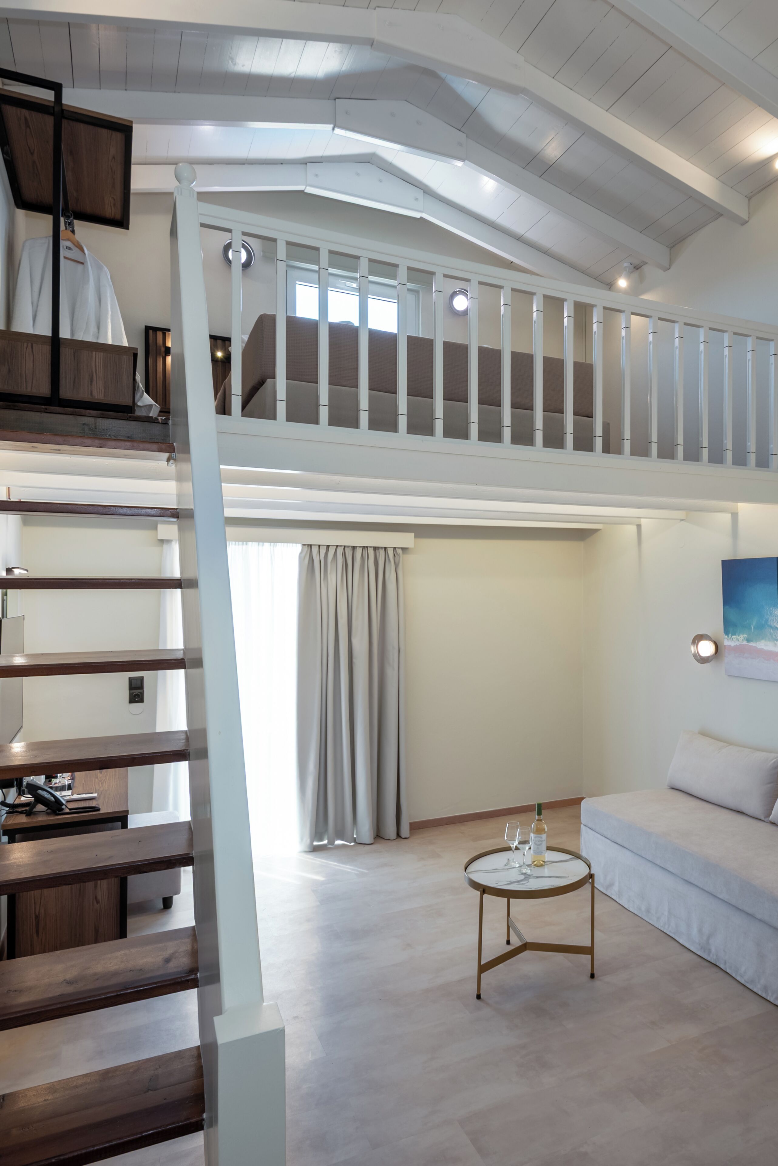 Un dormitorio estilo loft con una escalera, un sofá, una mesa redonda de centro y un cuadro en la pared.