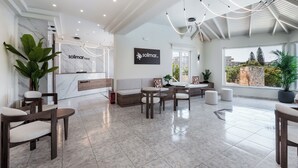 Un moderno hall de hotel con suelo de mármol, zonas de estar y un amplio ventanal con vistas al exterior.