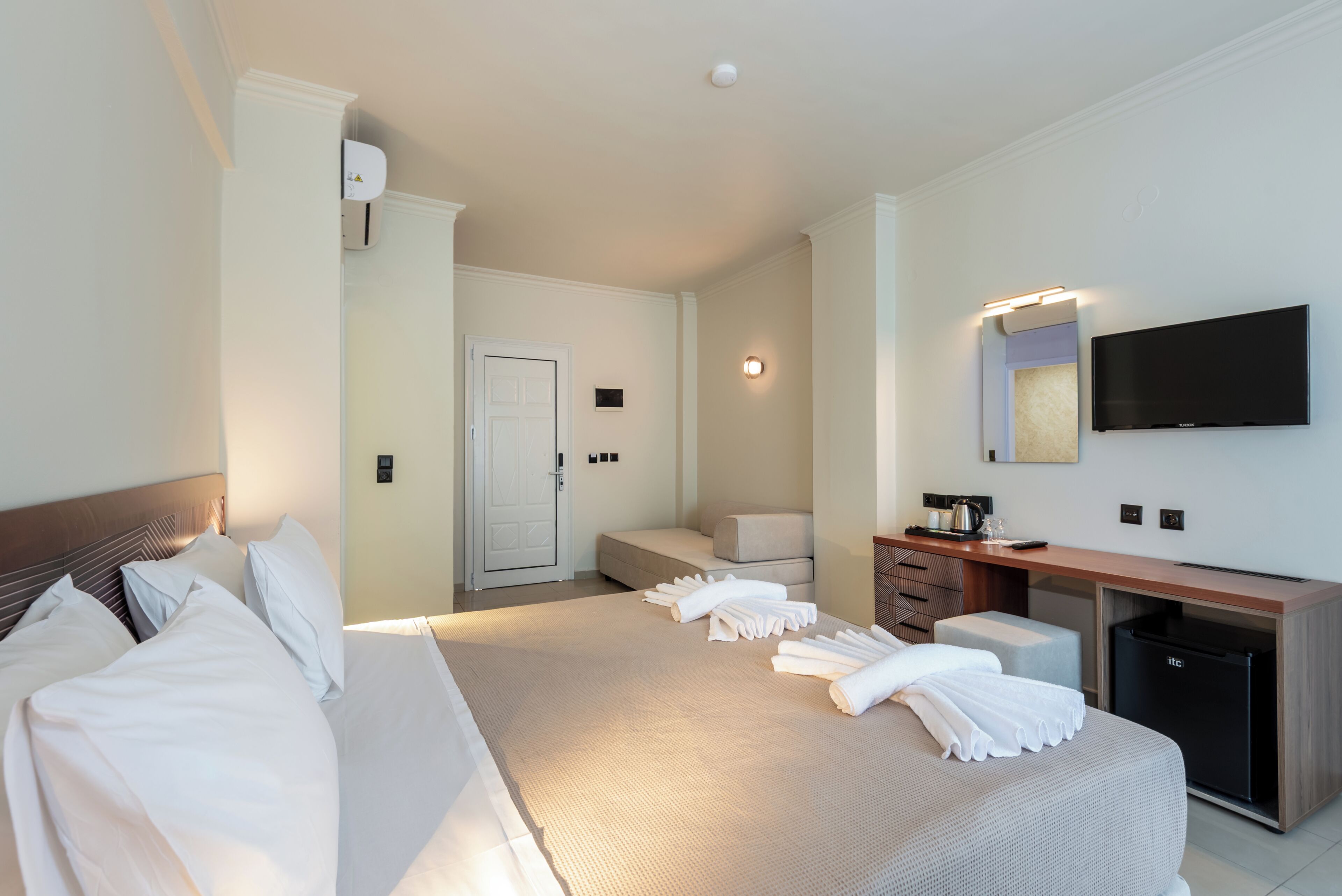 Habitación de hotel con una cama grande, un escritorio con televisor de pantalla plana, un minibar y una puerta que da a otra habitación.