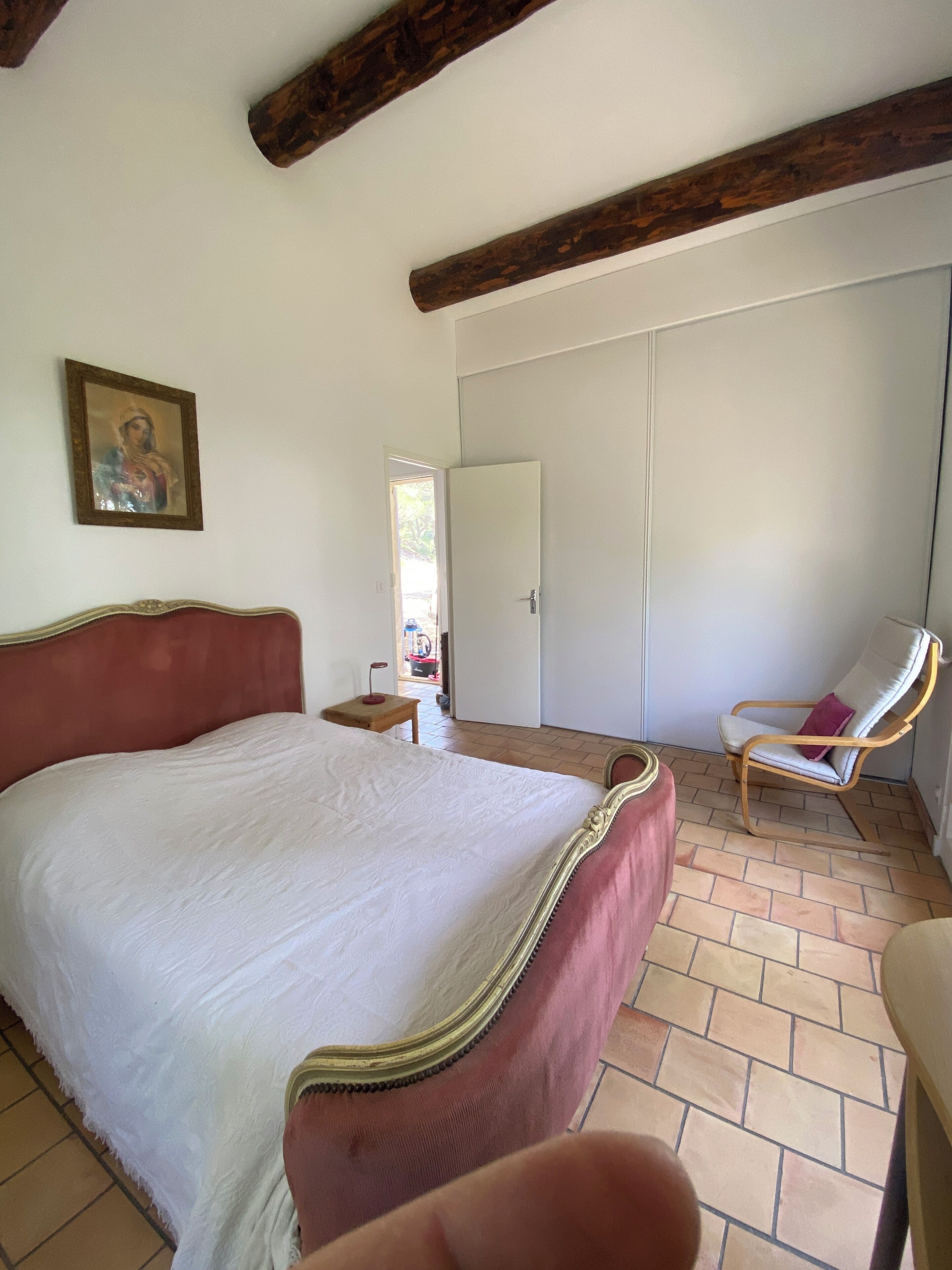 A bedroom with a bed, a chair, a wardrobe, and a door leading to a balcony.