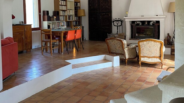 A spacious living area with a fireplace, a dining table with chairs, a bookshelf, and a red sofa. - La Grande Bastide (Grambois)