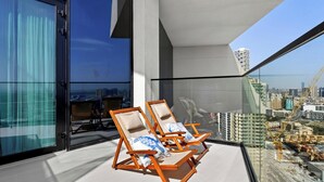 Ein Balkon mit zwei Holzliegen, einer Glastür und Blick auf die Stadt.