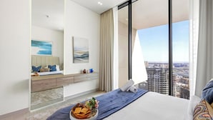 Ein modernes Hotelzimmer mit einem großen Bett, einem Nachttisch mit einer Snacksammlung, einem großen Spiegel und Blick auf die Stadt.