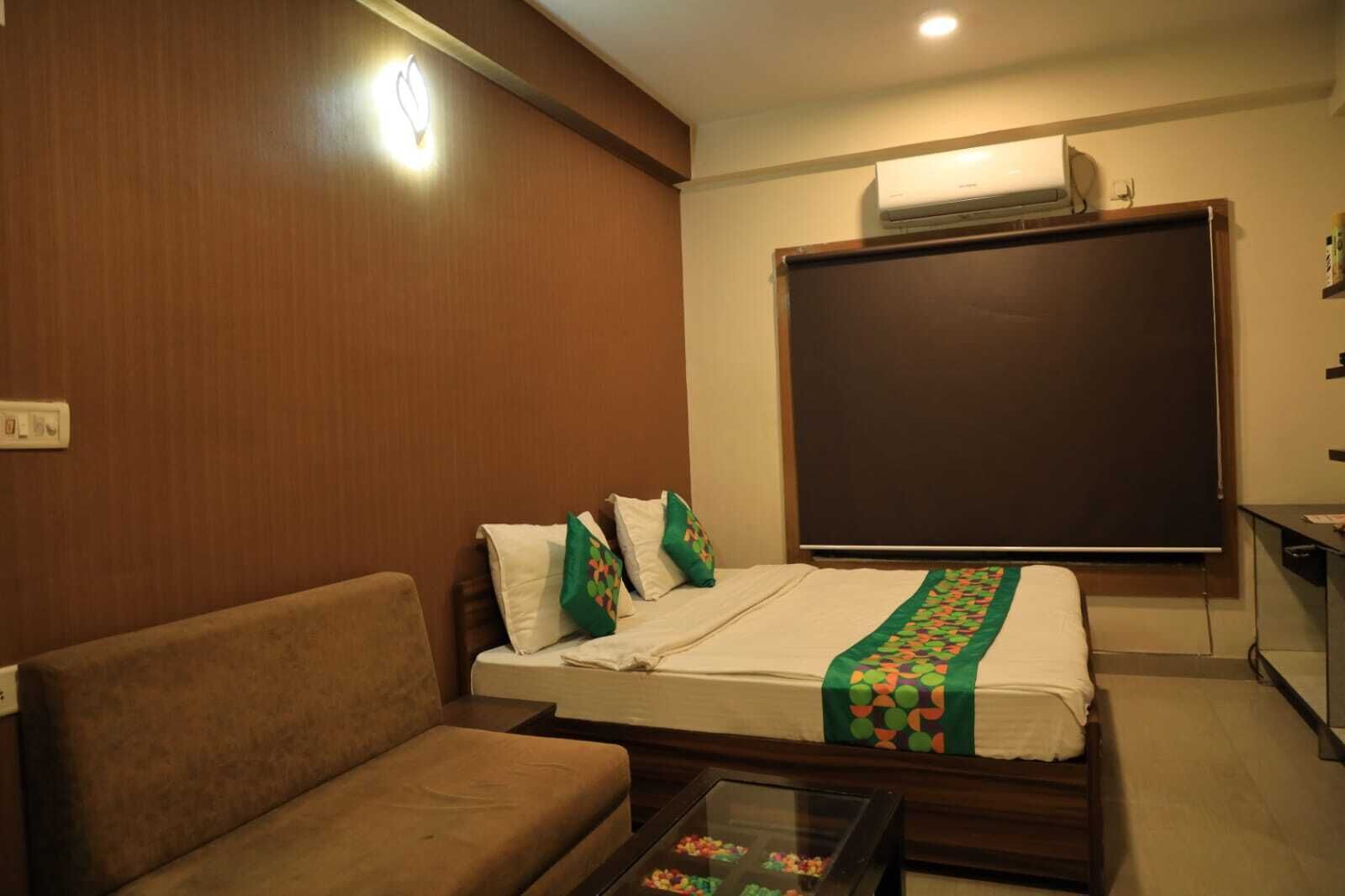 A room with a bed, a sofa, a small table with a glass top, and a wall-mounted air conditioner.