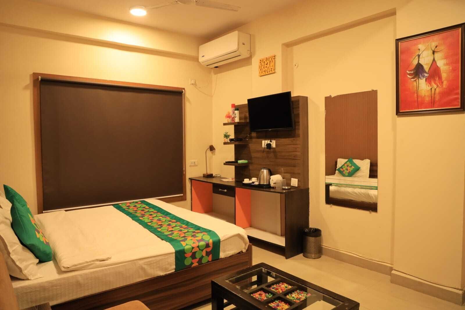 A hotel room with a bed, a desk, a television, a trash bin, and a painting on the wall.