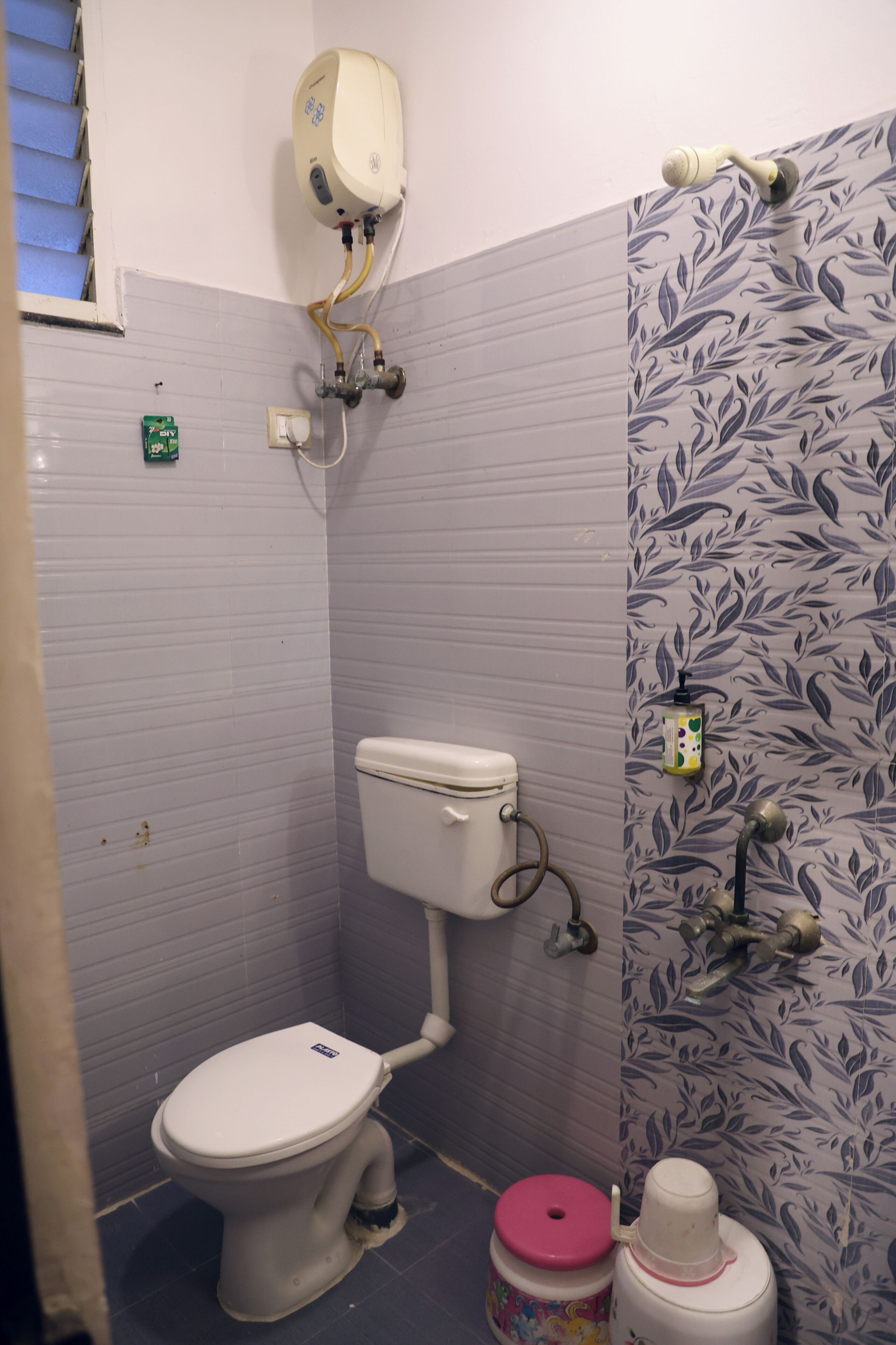 Et badeværelse med toilet, vandvarmer og bruser med et blomstret flisemønster.