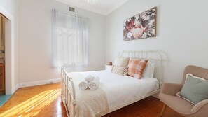 Ein Schlafzimmer mit einem Bett, einem Sessel, einem Fenster mit Vorhängen und einem Bild an der Wand.