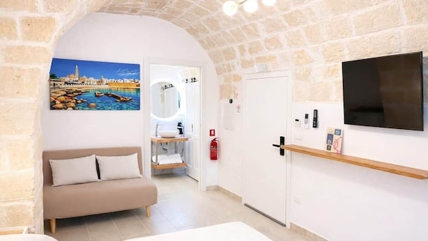 Een kamer met een stenen muur, een aan de muur bevestigde televisie, een bank, een kleine tafel en een schilderij van een kustlandschap.