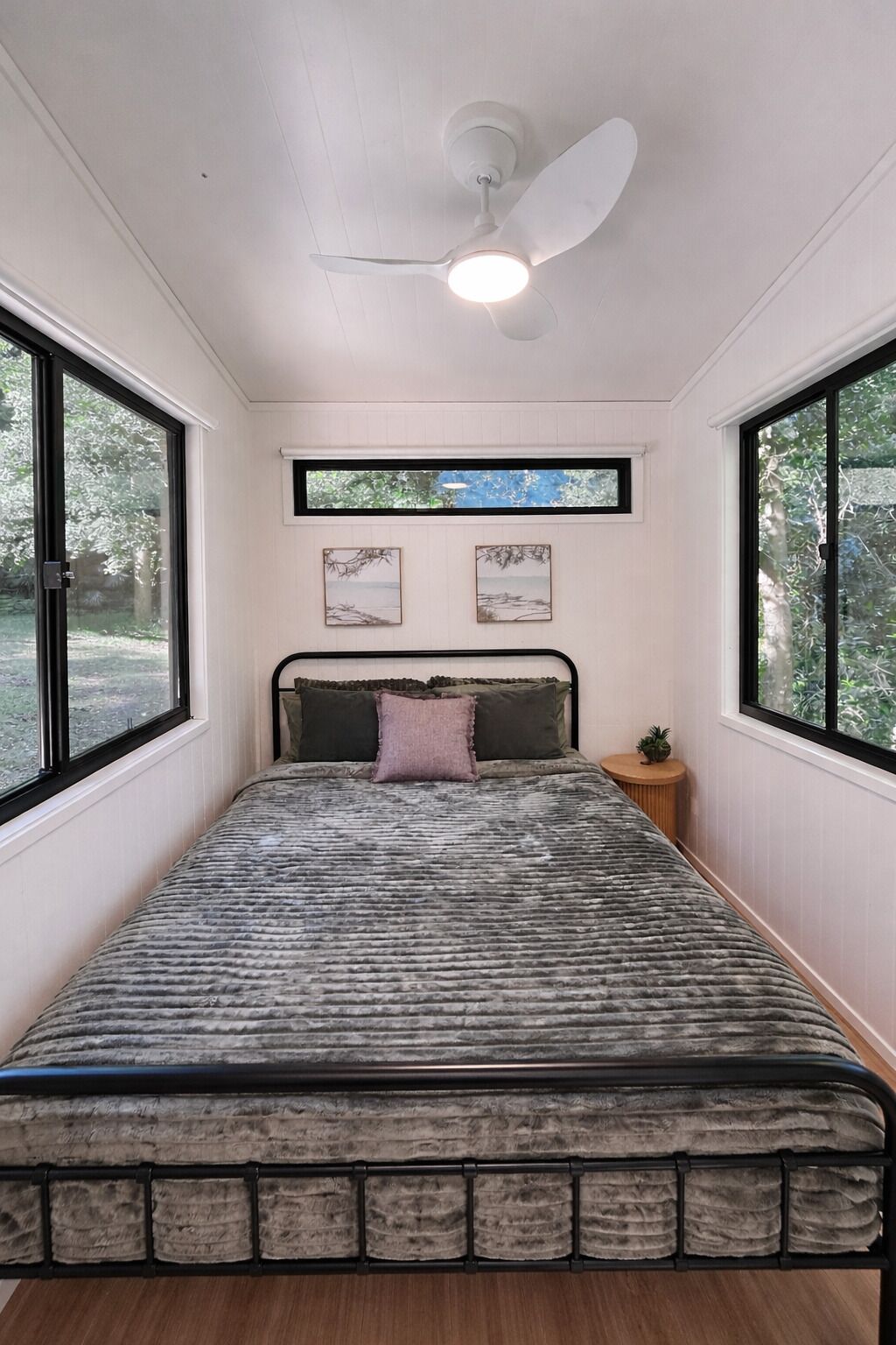 A bedroom with a bed, a ceiling fan, a window, and a small plant on a nightstand.