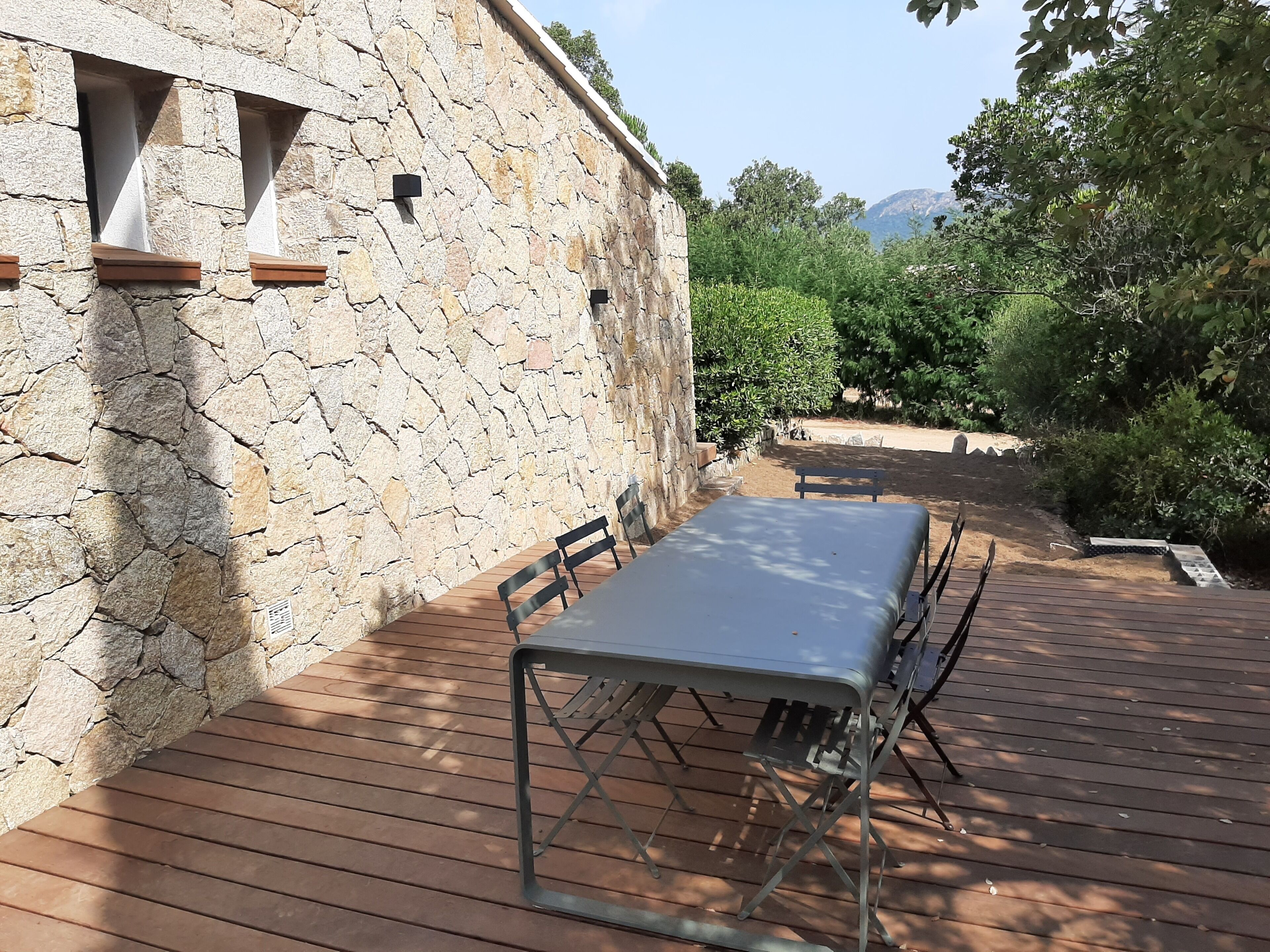 A stone wall with a table and chairs, a bench, and a view of trees and mountains.