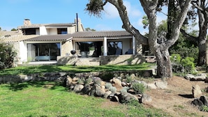 Une maison en pierre dotée d’un patio, d’un espace salon extérieur et d’un jardin agrémenté de rochers et de verdure.