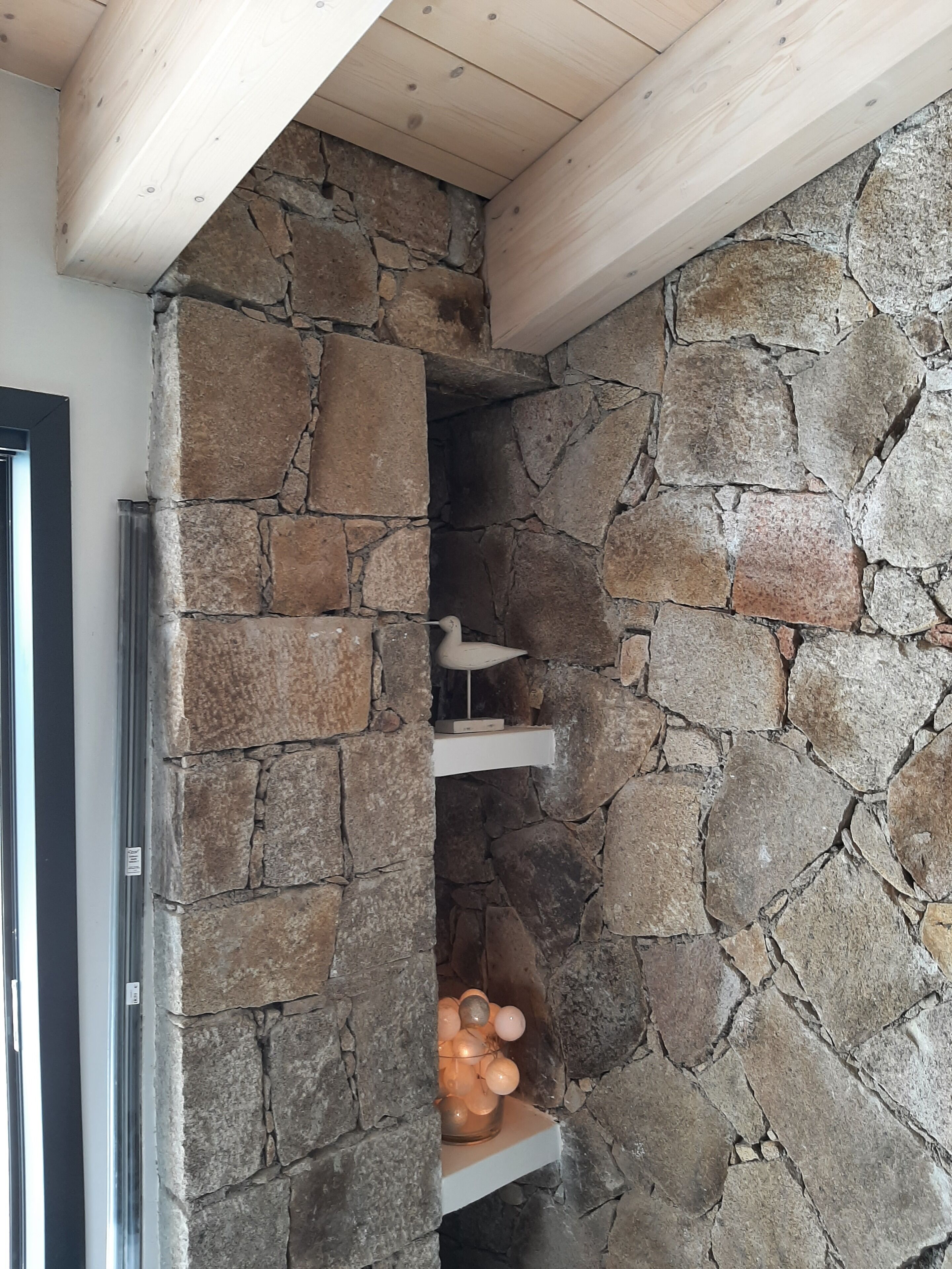 Ein Kamin aus Stein mit Ablage darunter, eine Holzbalkendecke und eine Tür links.