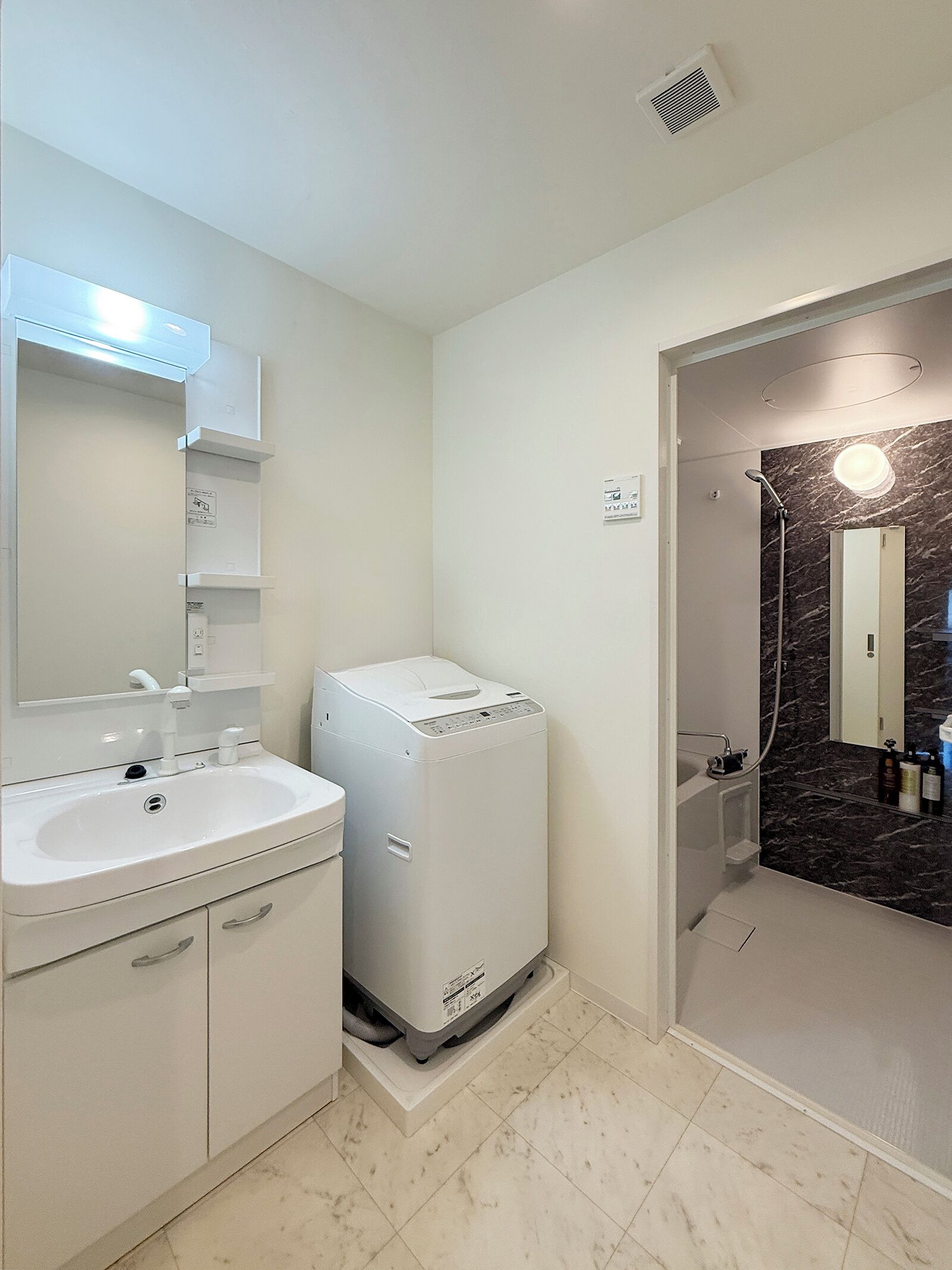 A bathroom with a white sink, a washing machine, a mirror, and a shower area.
