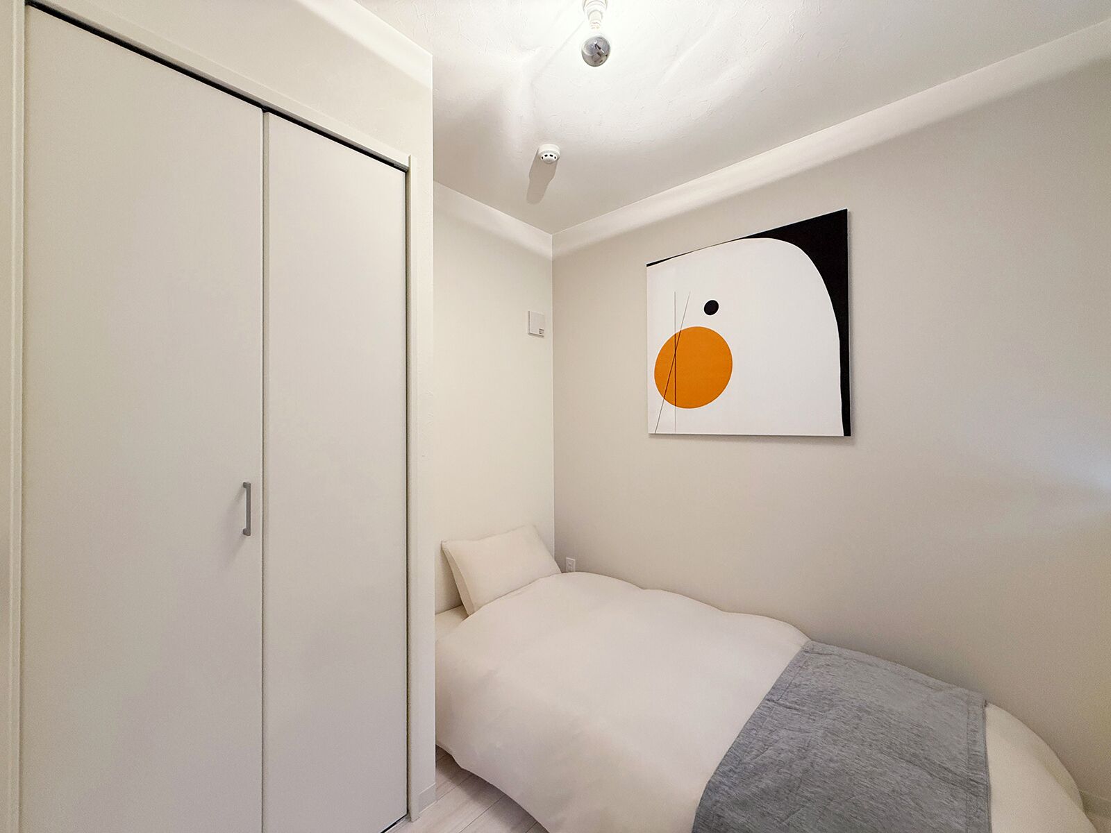 A bedroom with a bed, a wardrobe, and a wall-mounted artwork.