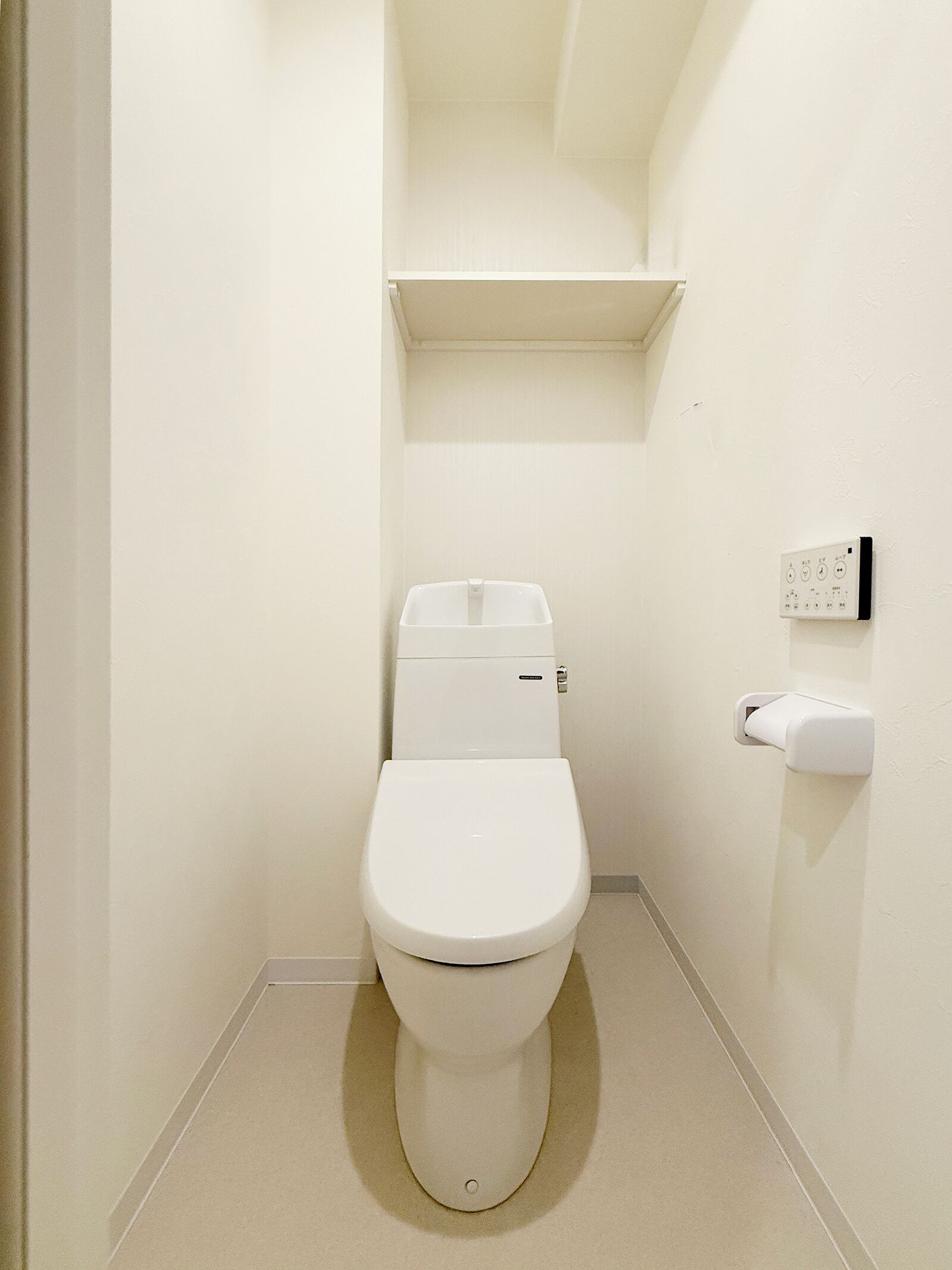 Ein kleines, weißes Badezimmer mit Toilette, einem Wandspülknopf und einem Regal darüber.