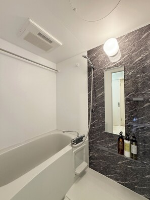 Un baño moderno con una bañera independiente, pared de mármol, un espejo grande y un cabezal de ducha.