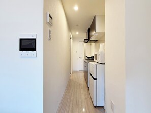 A narrow hallway with a kitchen area on the right, featuring a microwave, stove, and refrigerator. - GRACE TOUKAICHI (Hiroshima City)