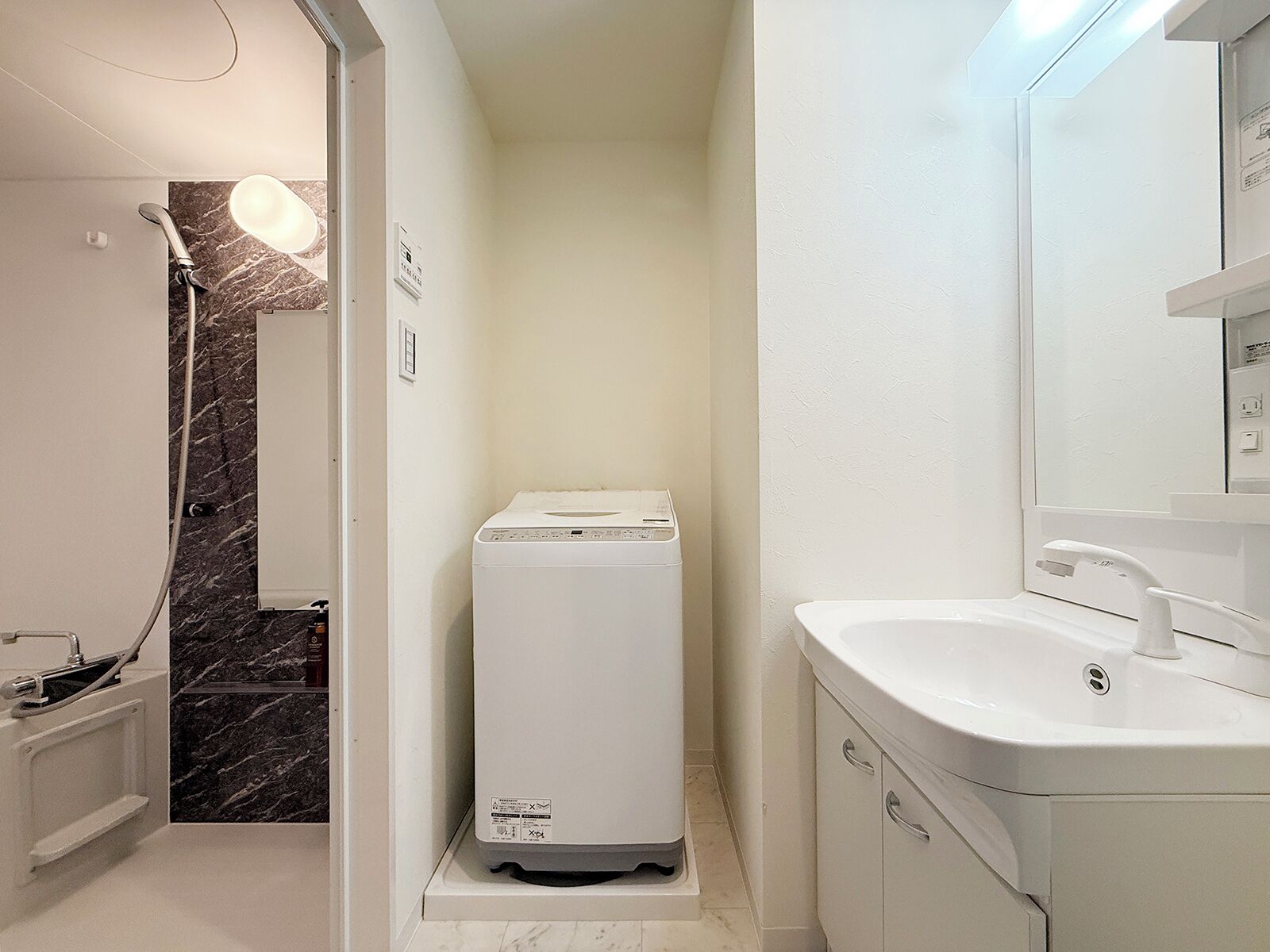 A compact bathroom with a shower, a white washing machine, and a sink with a mirror.