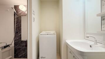 A compact bathroom with a shower, a white washing machine, and a sink with a mirror.