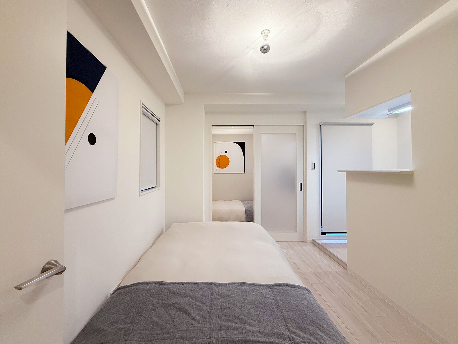 Una habitación de hotel moderna con una cama, una puerta, una obra de arte colgada en la pared y un pasillo que conduce a otra habitación.