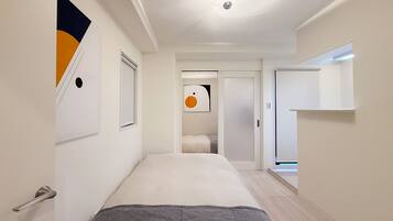 Una habitación de hotel moderna con una cama, una puerta, una obra de arte colgada en la pared y un pasillo que conduce a otra habitación.
