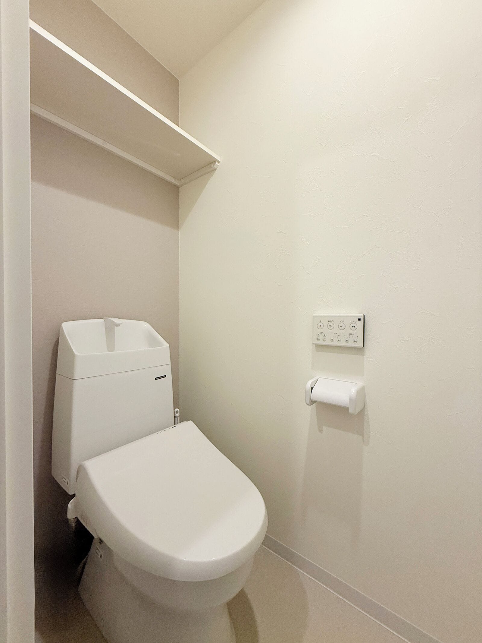 Een kleine, schone badkamer met een toilet, een papieren handdoekdispenser en een stopcontact op de muur.