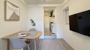 Et moderne køkken med et fladskærms TV, et spiseområde med bord og stole, og en gang der fører til en opholdsstue.