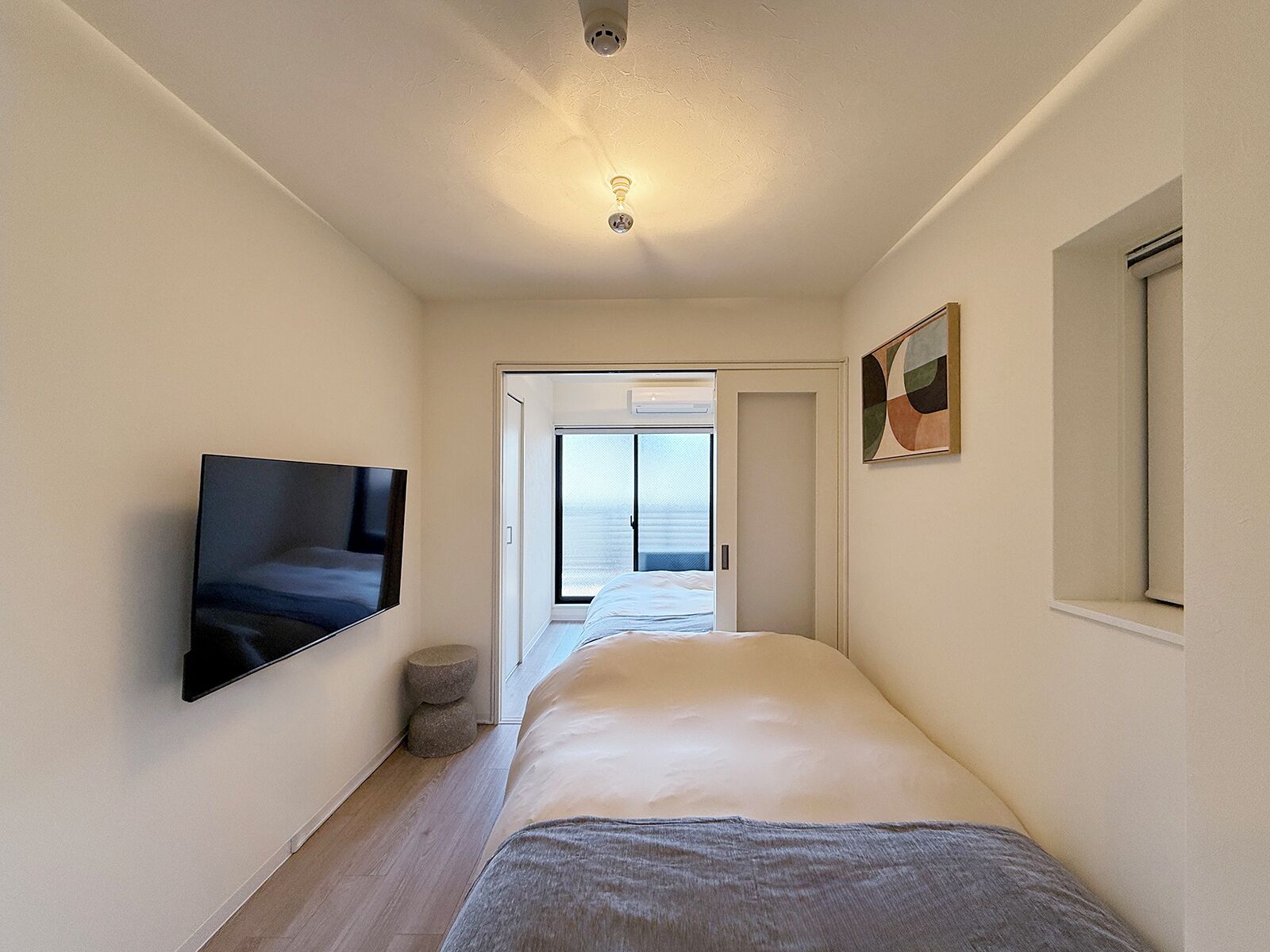 A narrow hallway with a bed, a television, and a door leading to a balcony.
