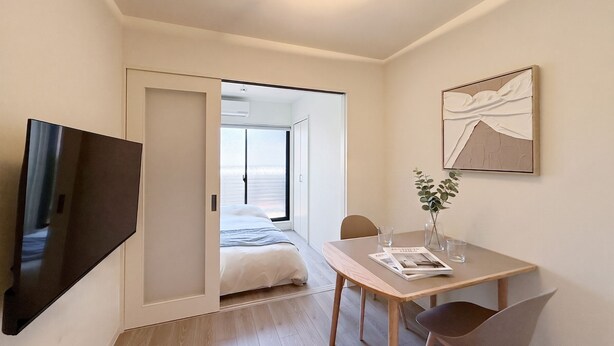 Et moderne hotelværelse med seng, fjernsyn, spisebord med stole og et stort vindue.