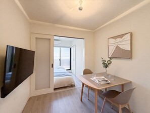 Una habitación de hotel moderna con cama, televisión, mesa de comedor con sillas y un ventanal grande.