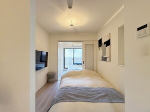 Ein schmales Hotelzimmer mit Bett, Fernseher, einem kleinen runden Hocker und Meerblick durch eine Tür.
