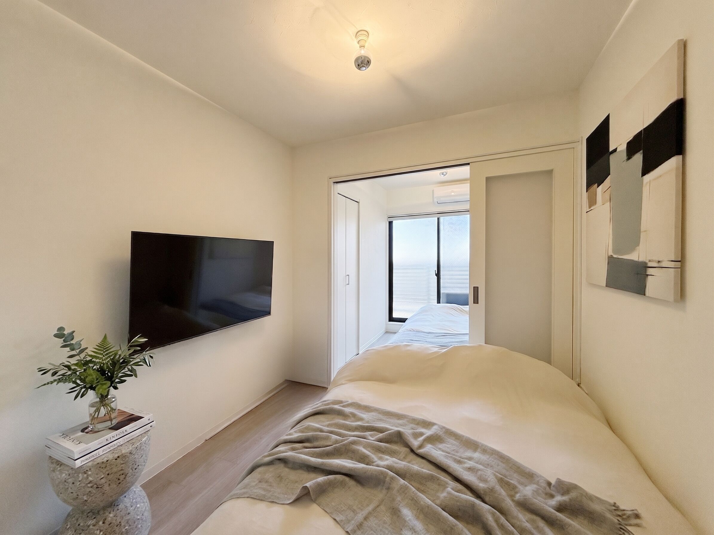 Un dormitorio con cama, televisor de pantalla plana, planta en maceta y vista a través de una puerta abierta.