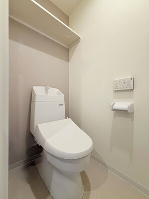 Eine weiße Toilette mit Tank, einem an der Wand befestigten Toilettenpapierhalter und einem Regal darüber.