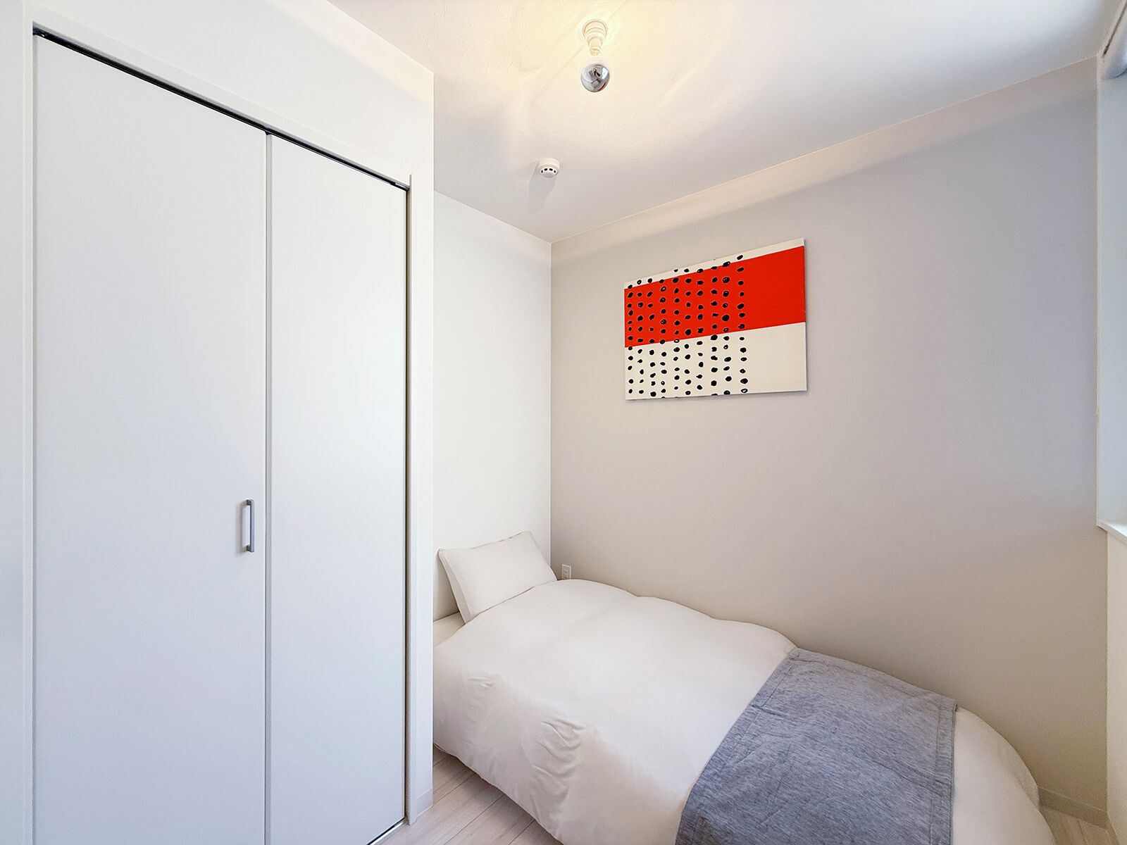 A bedroom with a bed, a wardrobe, and a wall-mounted artwork.