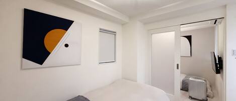 Una habitación de hotel moderna con una cama grande, una obra de arte colgada en la pared, un radiador y una puerta que da a otra habitación.