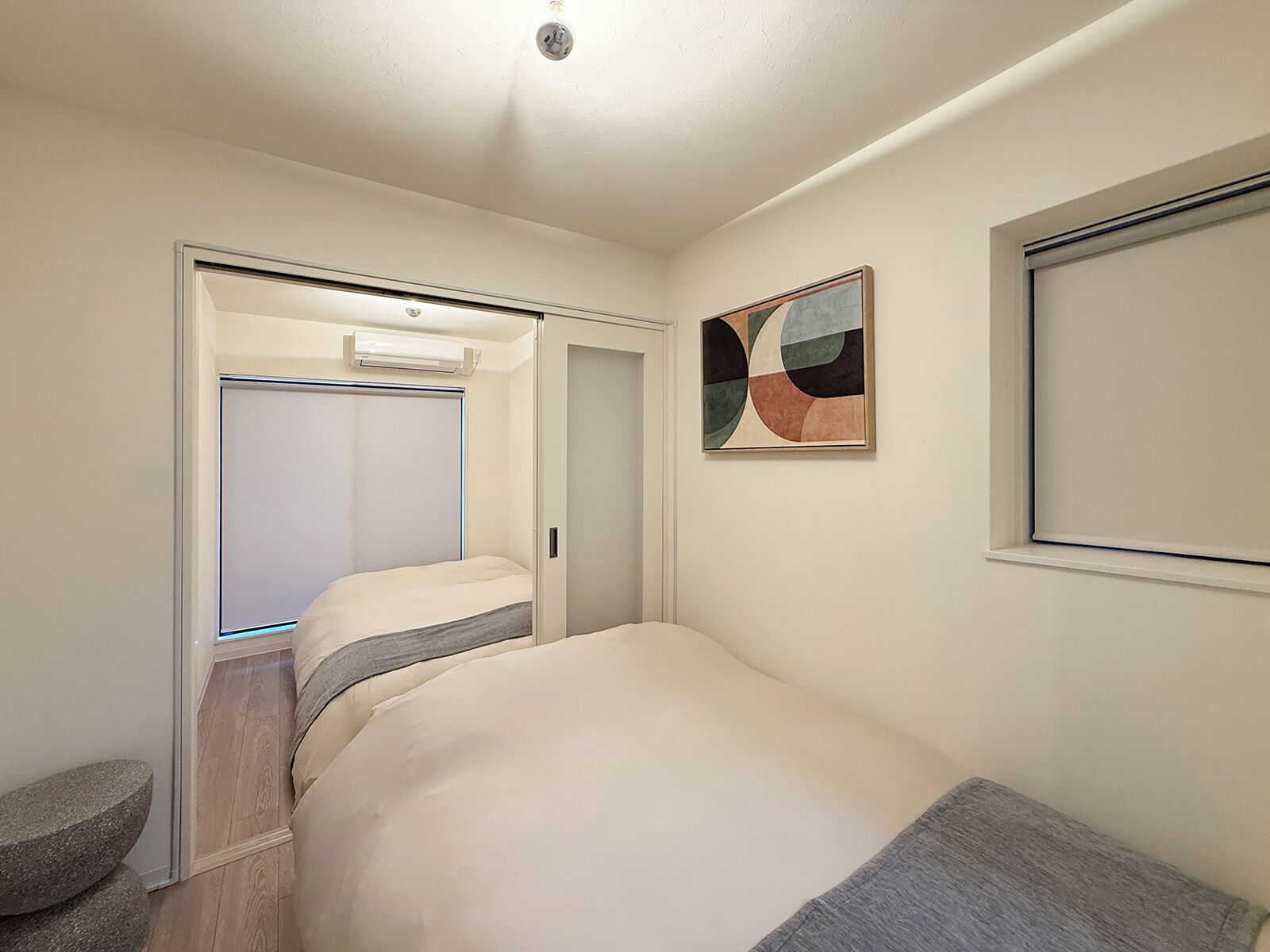 A bedroom with a bed, a wardrobe, a door, a wall-mounted artwork, and a window.