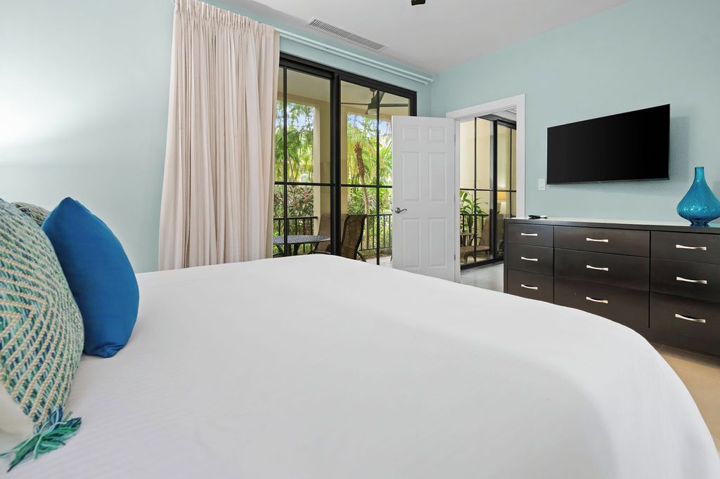 A bedroom with a large bed, a dresser, a television, and a sliding glass door leading to a balcony.