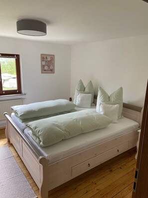 A double bed with two pillows, a bedside table, a window, and a wall-mounted light fixture.