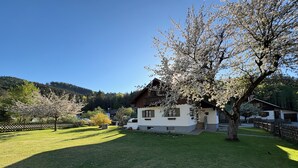 Uma casa com telhado inclinado, cerca de madeira e uma árvore em primeiro plano.
