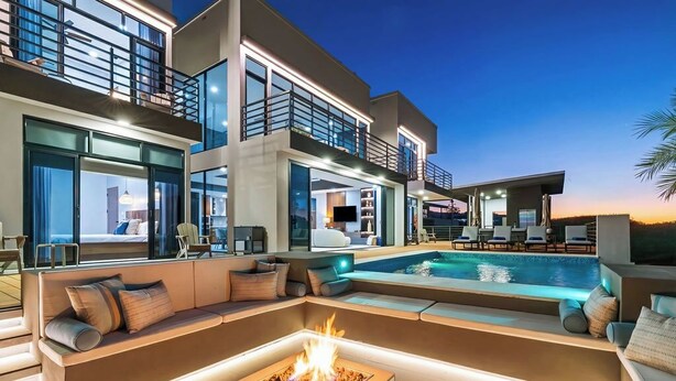 Ein modernes, mehrgeschossiges Haus mit Pool, Sitzgelegenheiten im Freien und einem Feuerkorb.