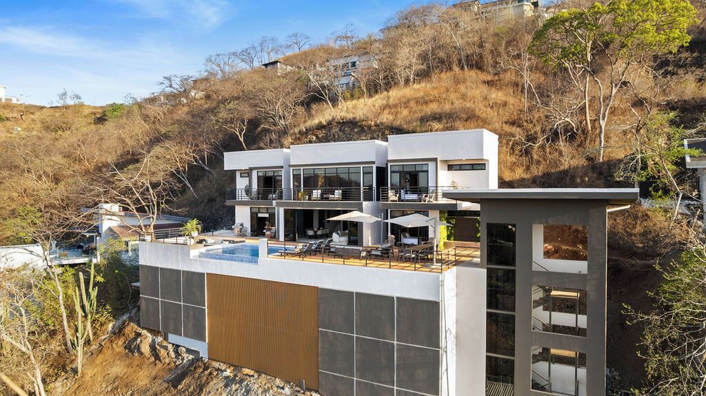 Un edificio moderno a più piani con area piscina sul tetto, ampie finestre e uno sfondo collinare.