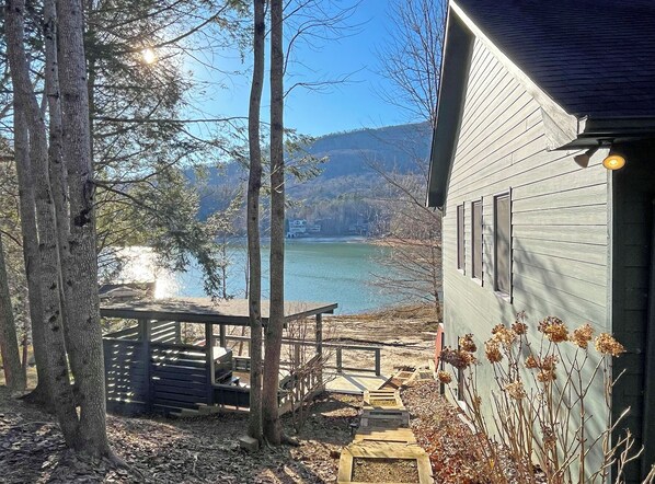 Mökki, jossa on terassi, jolta avautuu näkymä järvelle, ja jonka ympärillä on puita.
