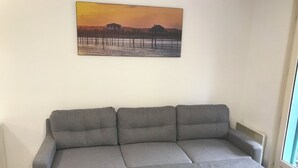 Un sofá gris en una habitación con un cuadro colgado en la pared que representa una puesta de sol.